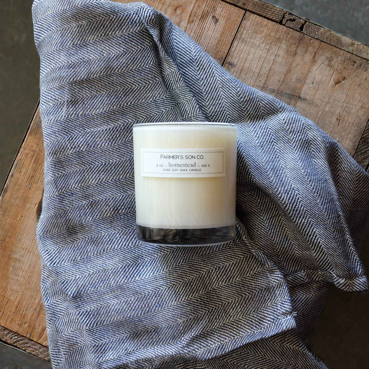 Homestead 8oz candle resting on linen towel from Farmer's Son Co.