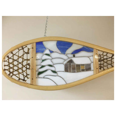Stained glass art in a snow shoe featuring a cabin under northern lights